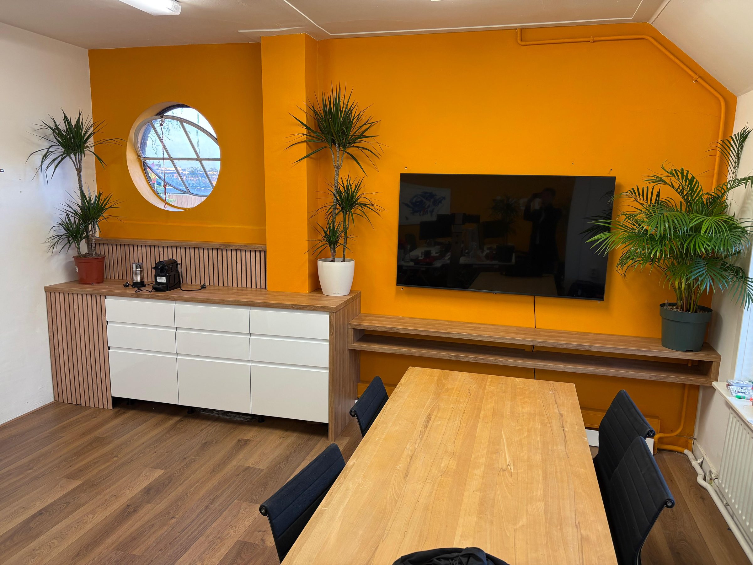 De vergaderruimte op het DotX-kantoor: oranje wand, rond venster en houten vergadertafel