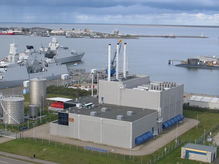 Kracht-warmtestation aan de haven van de marinebasis in Den Helder, met opslagtanks en marineschepen op de achtergrond