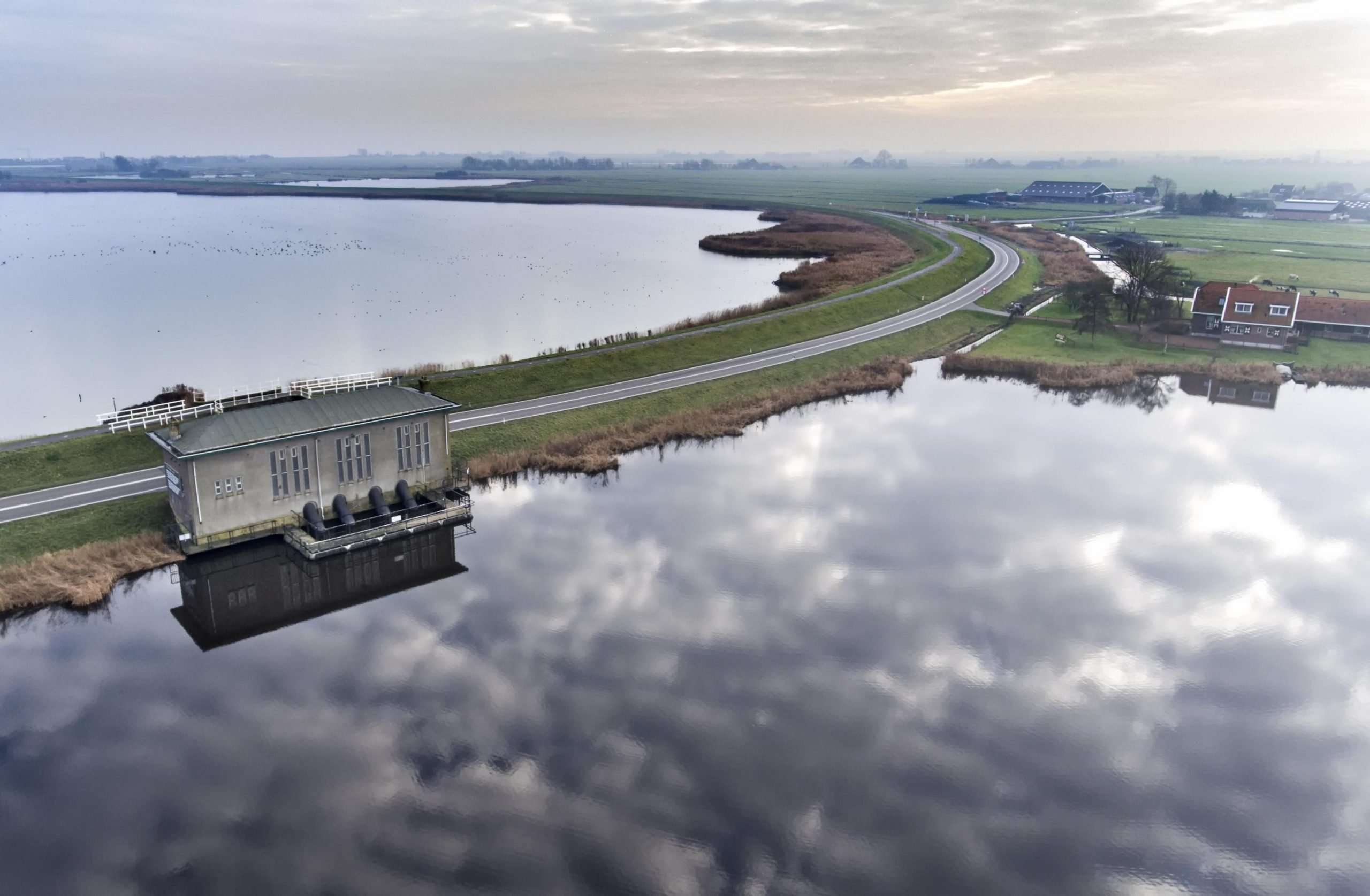 Gemaal in een polder, luchtopname boven het boezemwater met een weg over de dijk